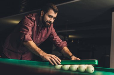 handsome man forming triangle of russian pool balls at bar clipart
