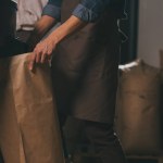 Partial view of worker in apron with paper bags of coffee beans