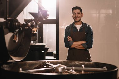 portrait of smiling coffee roaster standing at roasting machine and looking at camera clipart