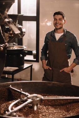 portrait of smiling coffee roaster standing at roasting machine and looking at camera clipart