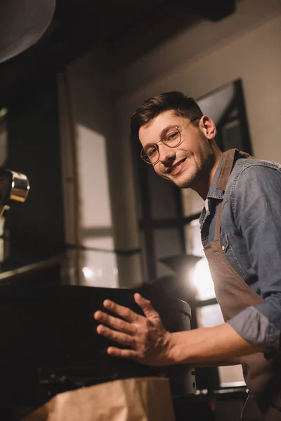 コーヒー ショップで働く若いコーヒー豆を炒るを笑顔の側面図 — ストック写真
