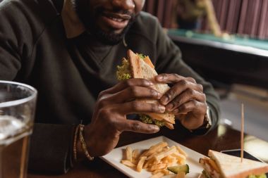 cropped image of african amercian man eating sandwich at bar clipart