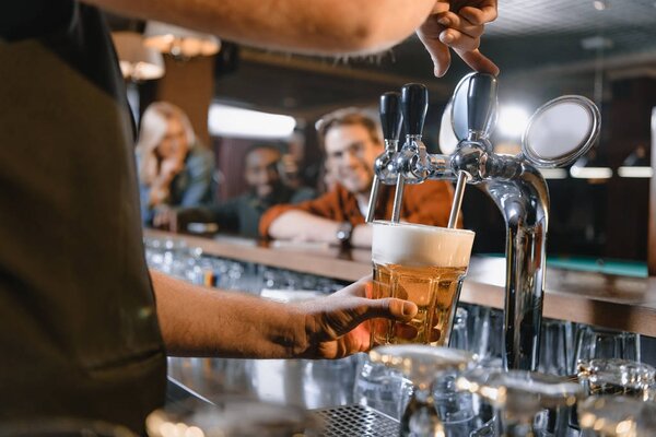 обрезанное изображение бармена, наливающего пиво в стекло в баре
