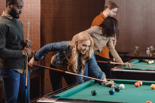 young attractive multiculture friends playing in pool at bar