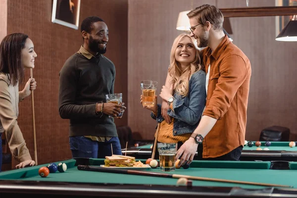 company of multiethnic friends eating and drinking beside pool table at bar