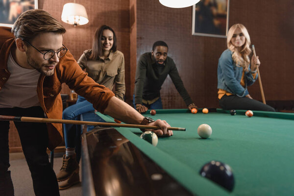 young attractive multiethnic friends playing in pool at bar