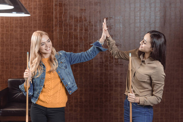 two young girls holding cues and giving high five to each other at bar