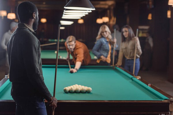 young multiethnic friends playing in pool at bar