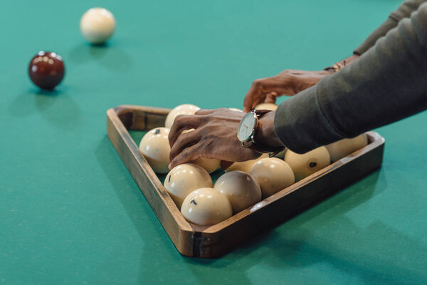 обрезанное изображение мужских рук, образующих шары, установленные треугольником на столе для игры в бильярд
 