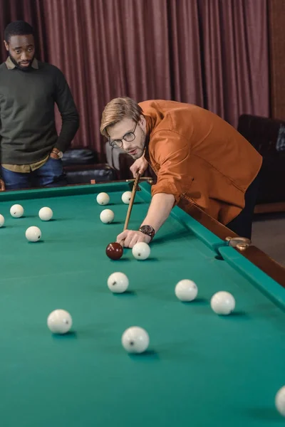 handsome man playing in pool at bar with friend
