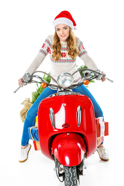 attractive woman in santa hat sitting on red scooter with gifts and christmas tree, isolated on white