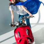 Mulher feliz em traje de super-herói e capacete de proteção em scooter vermelho