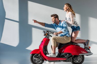 gülümseyen adam uzakta scooter kız arkadaşı ile birlikte üzerinde otururken işaret yan görünüm