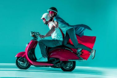 Çift birlikte kırmızı scooter sürme süper kahraman kostümleri yan görünüm