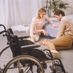Mann mit Behinderung und Frau spielen Schach im Schlafzimmer mit Rollstuhl im Vordergrund