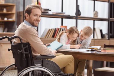 Baba evde çocuk eğitimi ve kameraya bakarak tekerlekli sandalye üzerinde gülümseyen