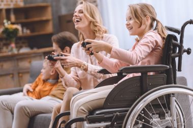 joystick ile birlikte evde oynarken tekerlekli sandalyede özürlü çocuk ile mutlu aile 