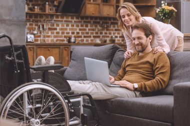 mutlu kadın bakarak bacaklar tekerlekli sandalye üzerinde koyarak ve dizüstü evde kullanma koca devre dışı