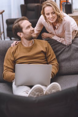 gülümseyen kadın bakarak bacaklar tekerlekli sandalye üzerinde koyarak ve dizüstü evde kullanma koca devre dışı