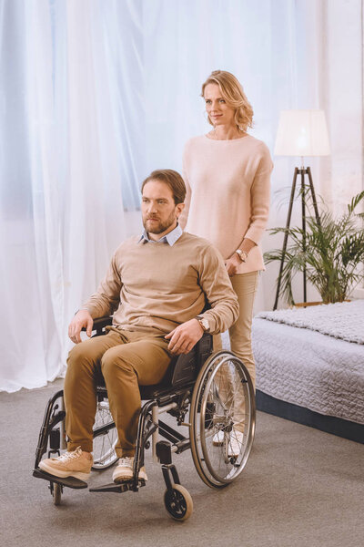 husband on wheelchair and wife looking away in bedroom