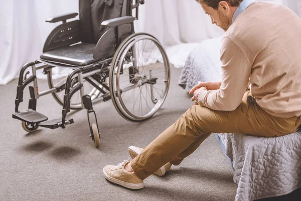 Smutny Człowiek Niepełnosprawnością Siedząc Łóżku Wózek Inwalidzki Stojący Pobliżu — Zdjęcie stockowe