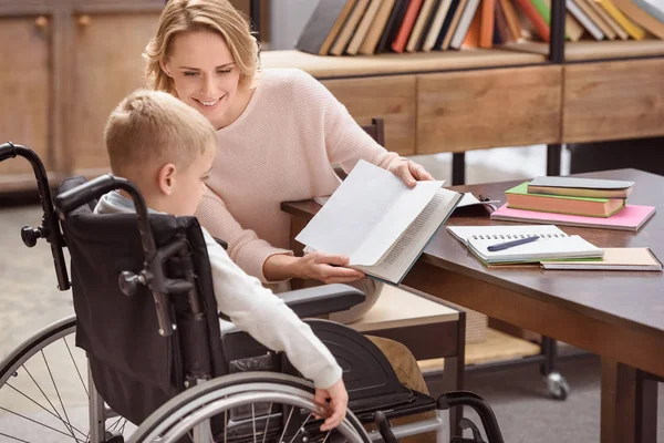 Mãe Feliz Mostrando Algo Livro Para Filho Cadeira Rodas — Fotografia de Stock