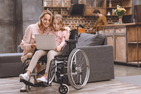 Mãe Sorridente Filha Pequena Cadeira Rodas Usando Laptop Juntos Enquanto — Fotografia de Stock