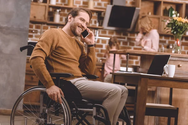 Uśmiechający Się Niepełnosprawny Człowiek Wózku Inwalidzkim Rozmawiając Smartphone Komputera Przenośnego — Zdjęcie stockowe