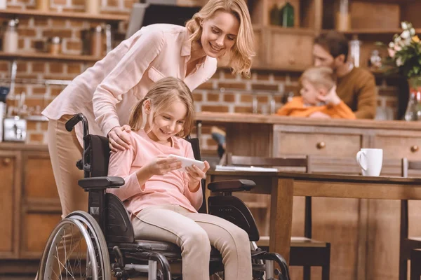 Happy Mother Looking Smiling Disabled Daughter Sitting Wheelchair Using Smartphone — Stock Photo, Image