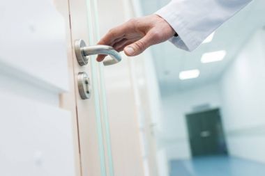 cropped view of male doctor holding door handle in hospital clipart