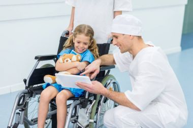tekerlekli sandalye üzerinde çocuk için bir şeyler tablete gösteriyor doktor