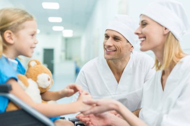Doktor ve hasta el ele tutuşarak tekerlekli sandalye üzerinde gülümseyen