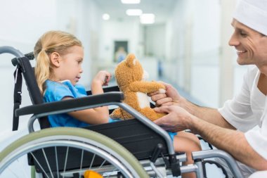 Doktor ve hasta el ele tutuşarak tekerlekli sandalye üzerinde yan görünüm