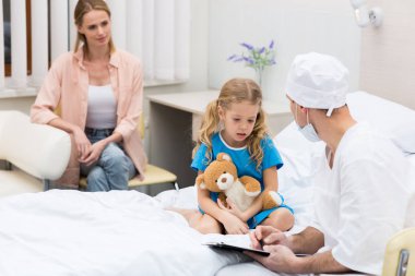 doctor talking with kid and sitting on hospital bed clipart