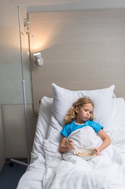 preschooler kid lying on bed in hospital with plate of oatmeal  clipart