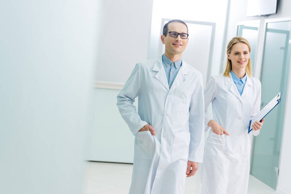 smiling doctors in white coats with diagnosis in hospital corridor