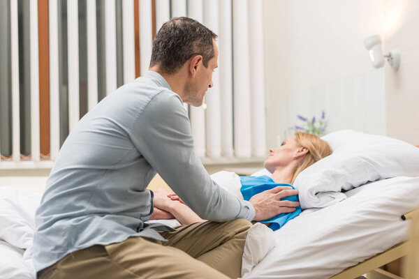 husband sitting at sick wife bed in hospital