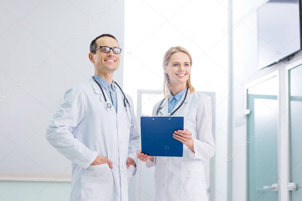 two cheerful doctors in white coats with stethoscopes and diagnosis standing in clinic