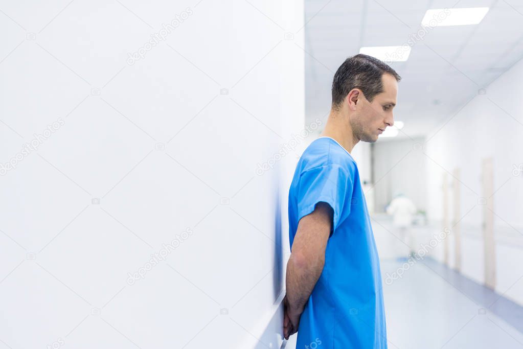 upset male patient in medical gown standing in hospital