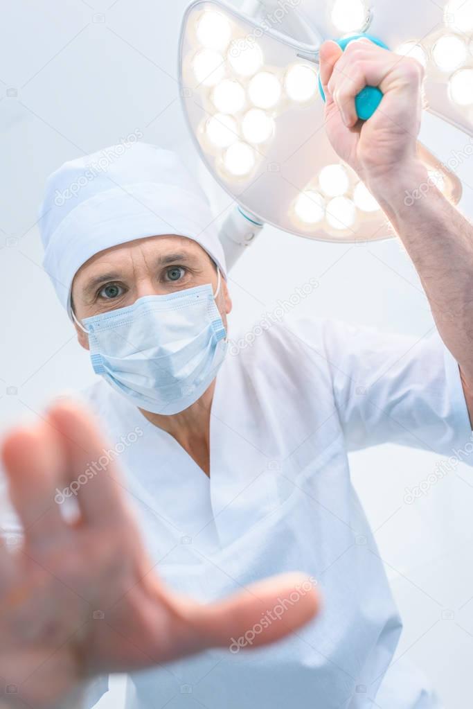 bottom view of doctor standing above patient in operating room and looking at camera