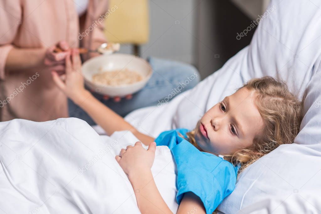 cropped image of sick kid rejecting food from mother