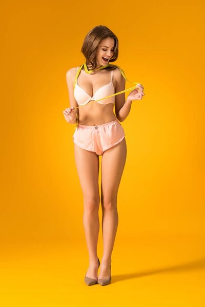 surprised sexy girl in lingerie set looking at tape measure on orange