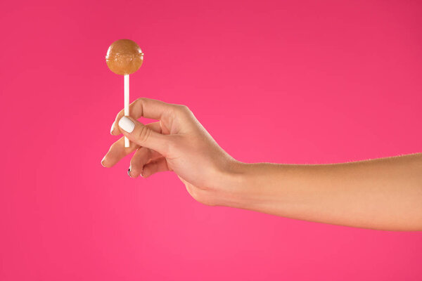 обрезанное изображение девушки, держащей в руке леденец, изолированный на розовый
