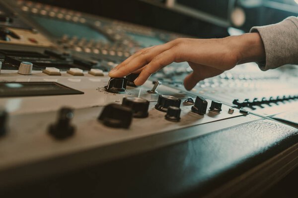 cropped shot of sound producer touching knobs on recording equipment