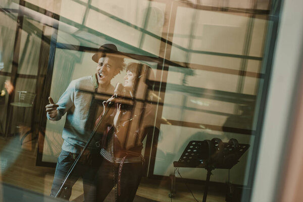 young talented singers couple recording song behind glass at studio