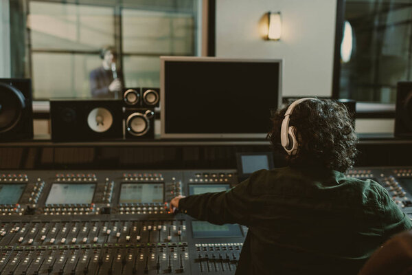 задний вид звукорежиссера, работающего в студии во время записи песни
