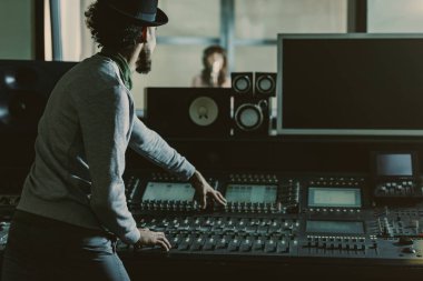 back view of sound producer in hat recording song at studio clipart