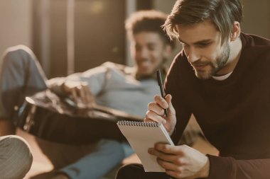 gitar ile yerde yatarken onun arkadaşı iken Not Defteri'nde şarkı sözleri yazmaya yakışıklı genç