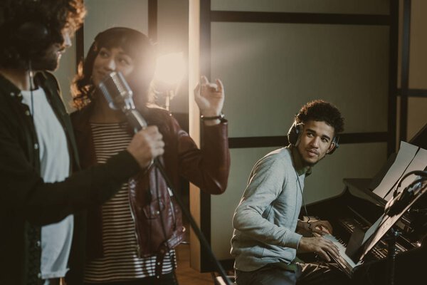 young couple performing song with microphone while man playing piano behind