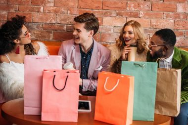 smiling fashionable multiethnic young people with shopping bags drinking coffee clipart